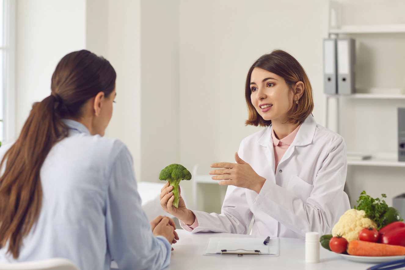 Nutritionist Holding Broccoli and Telling Young Woman about Benefits of Healthy Eating